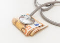 Health and medicine cost. Medical stethoscope on money, Euro banknote stack isolated on white, close up. Healthcare price in Europe