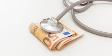 Health and medicine cost. Medical stethoscope on money, Euro banknote stack isolated on white, close up. Healthcare price in Europe